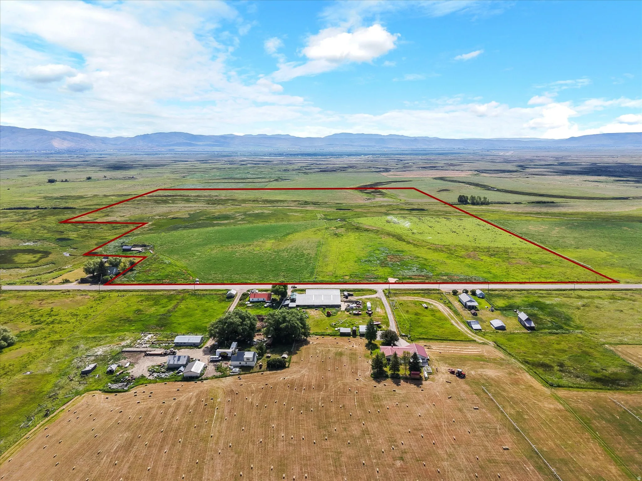 Expansive agricultural land featuring a mix of green fields and harvested hay bales, bordered by a road