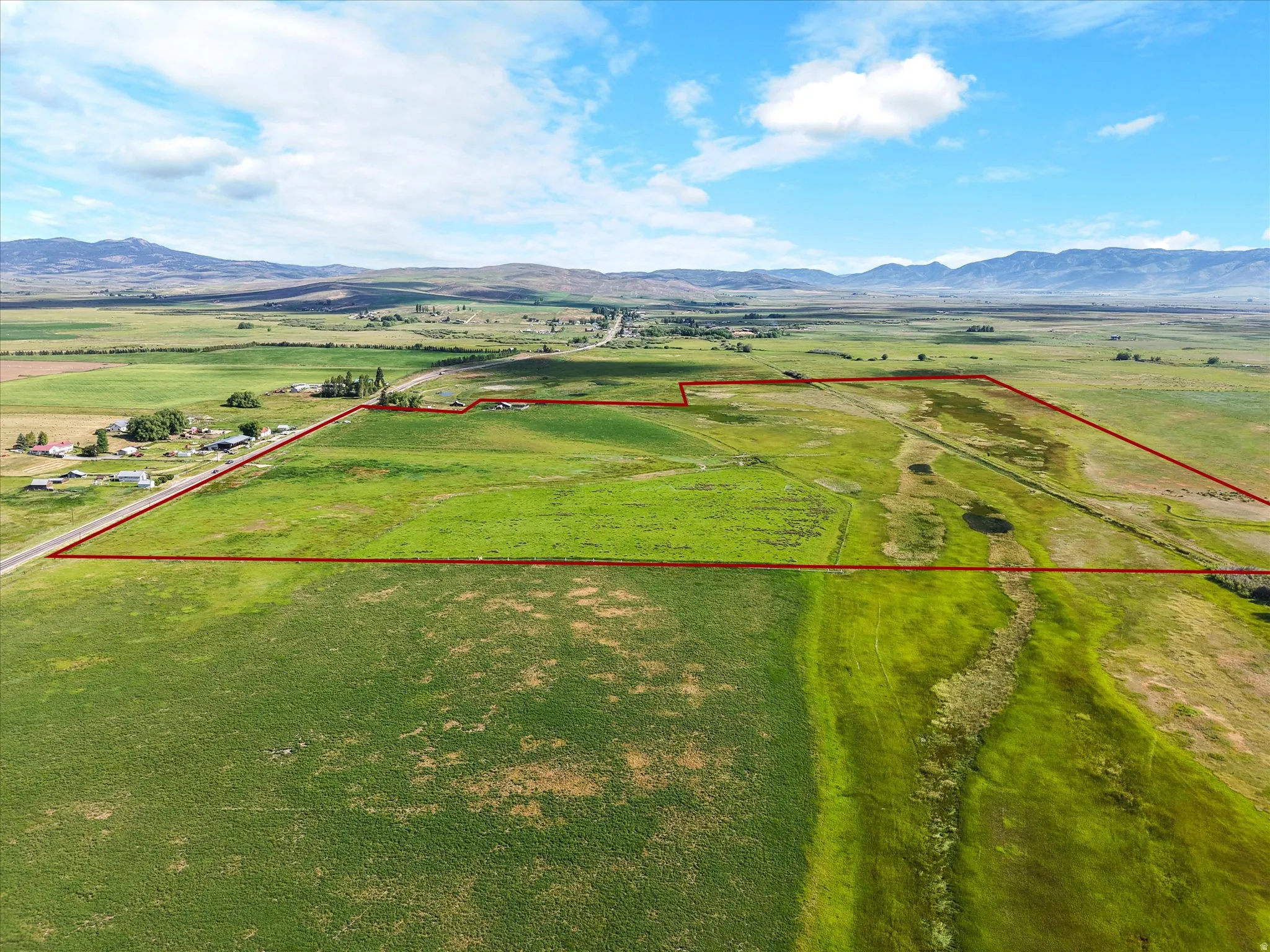 Expansive green acreage featuring a clear boundary outline, road frontage, and distant mountain backdrops