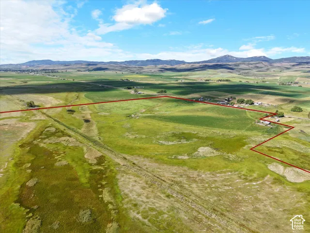Expansive rural acreage featuring green pastures, distant mountains, and scattered structures