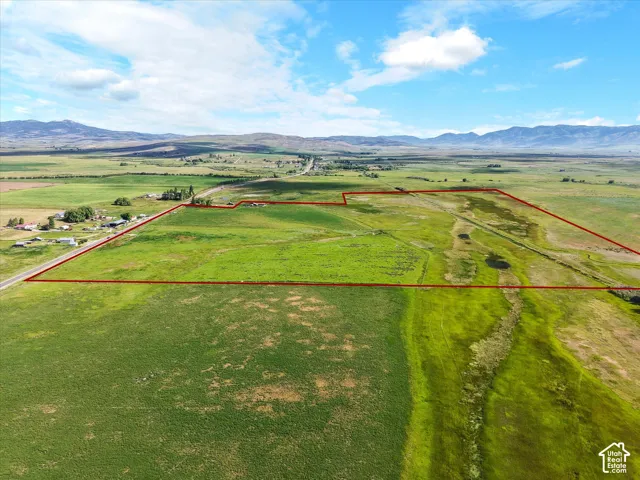 Expansive green acreage featuring a clear boundary outline, road frontage, and distant mountain backdrops