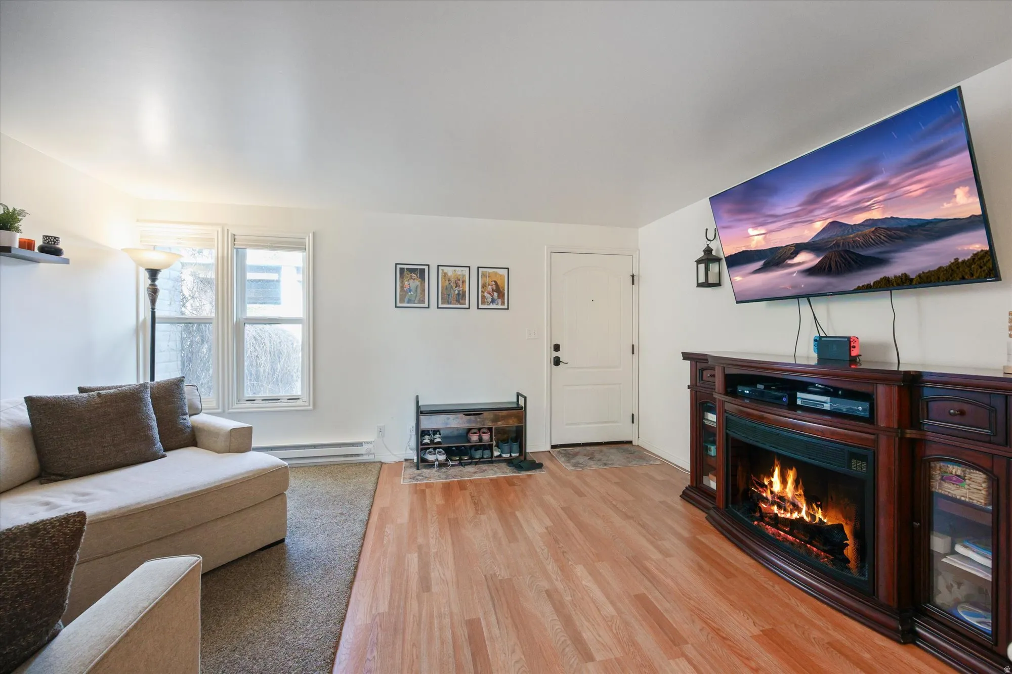 Living room with light wood-style floors, a warm lit fireplace, and a baseboard heating unit