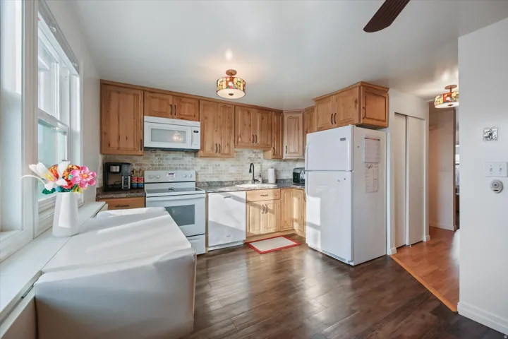 Kitchen featuring white appliances, dark wood-style floors, ceiling fan, wood finish cabinetry, and light countertops