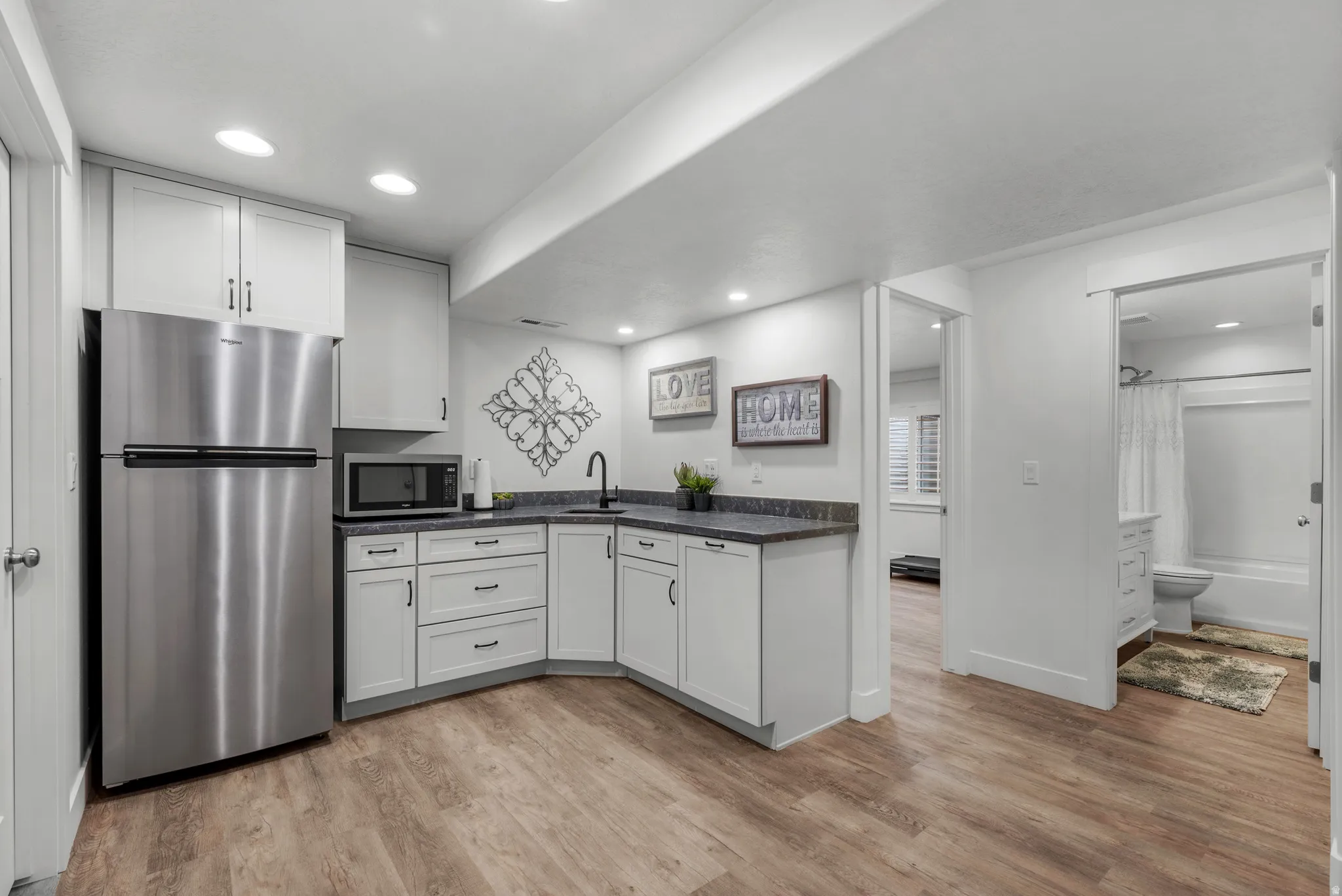 Kitchen featuring stainless steel appliances, light wood-style flooring, white cabinets, dark countertops, and recessed lighting