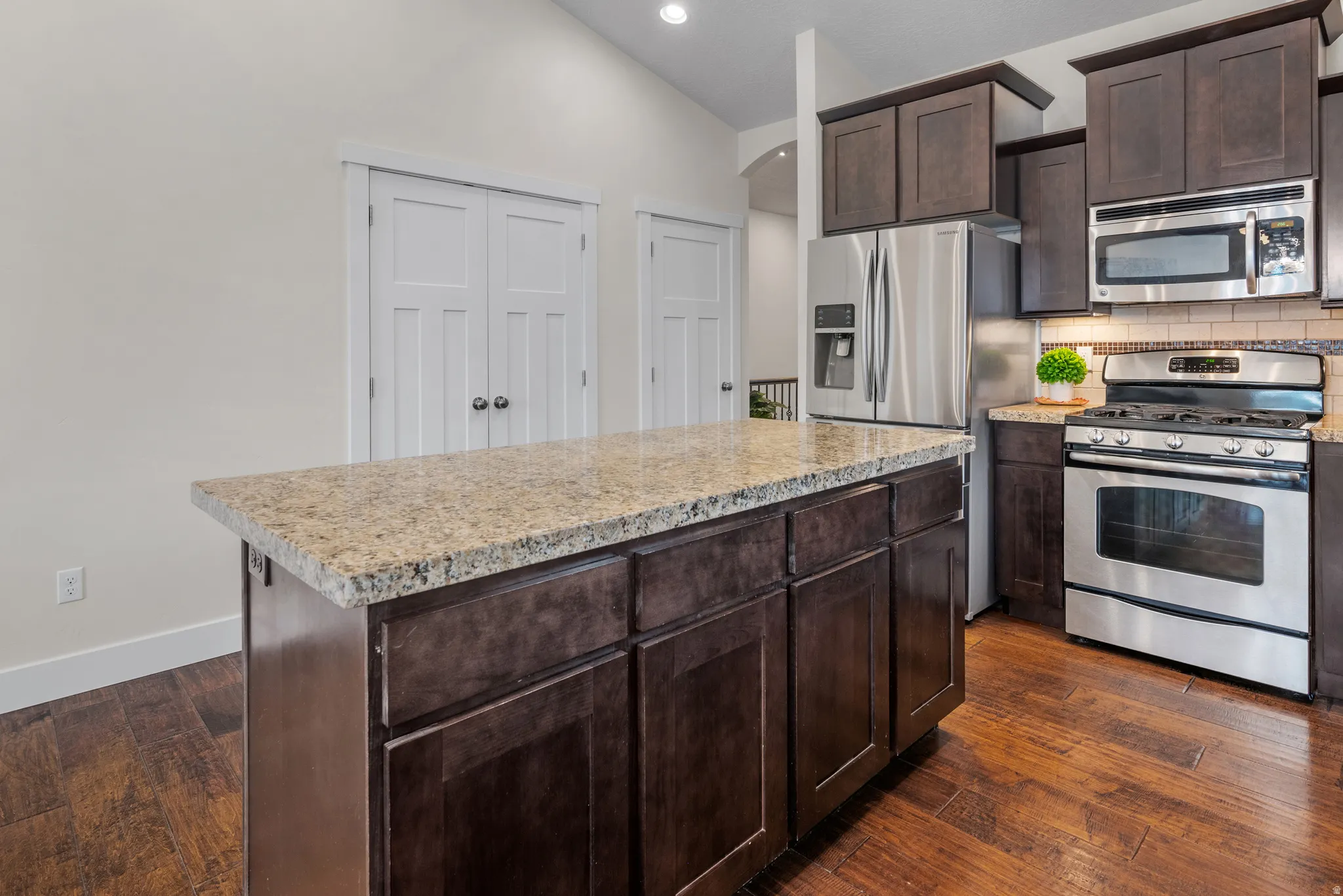 Kitchen featuring stainless steel appliances, dark wood finish cabinets, dark wood-style floors, backsplash, and vaulted ceiling