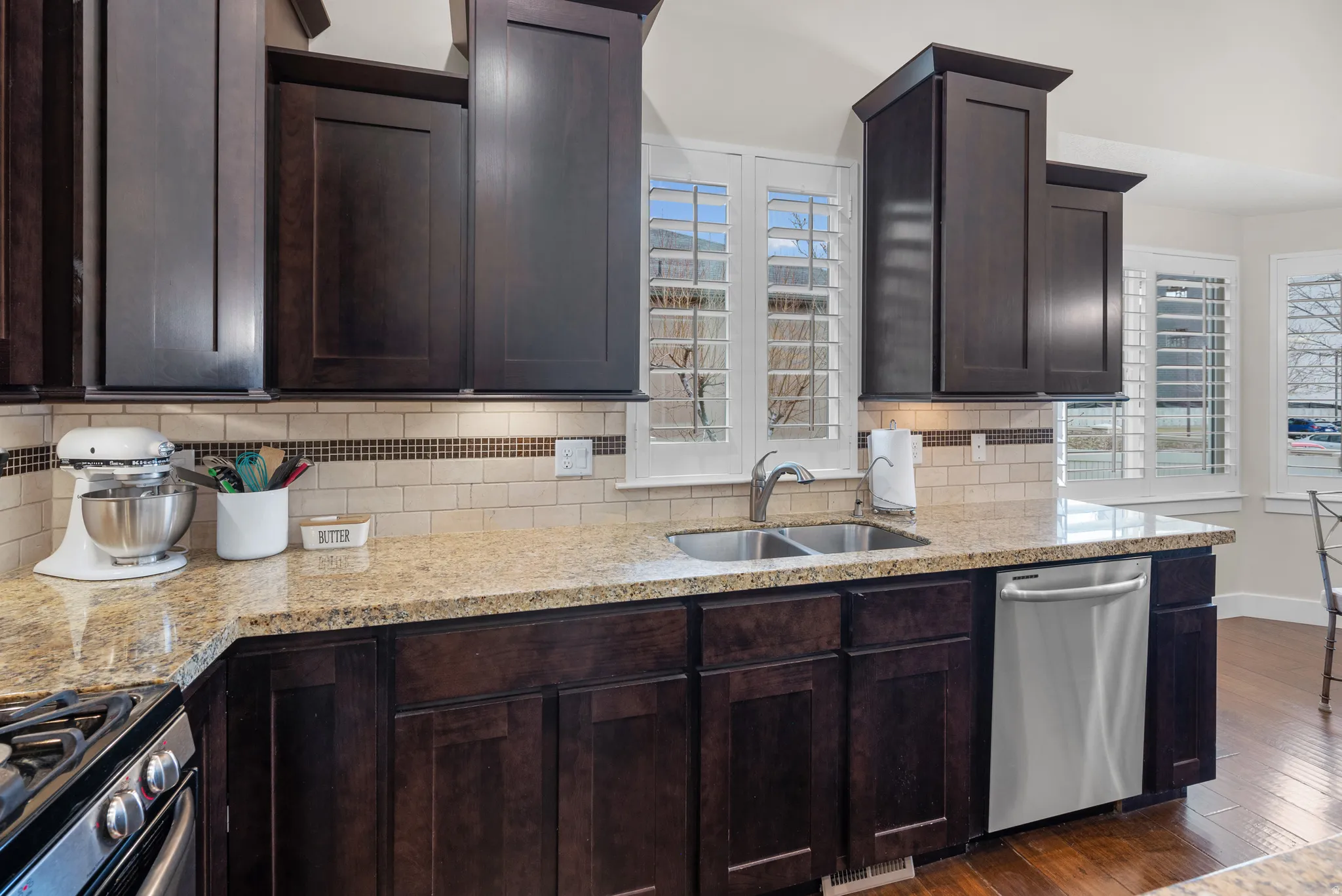 Kitchen featuring dark wood finish cabinetry, stainless steel appliances, dark wood-style flooring, and light stone countertops
