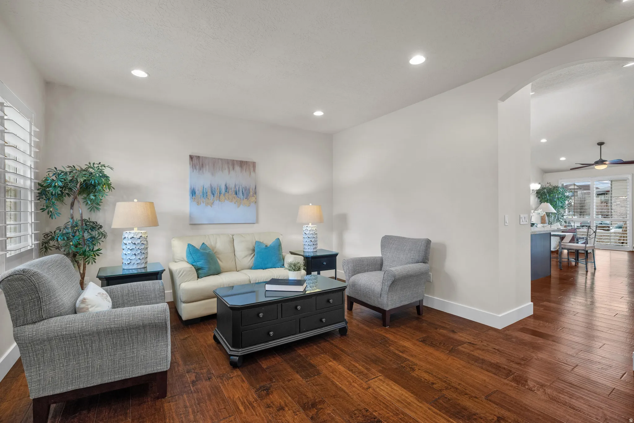 Living room with dark wood-type flooring, arched walkways, a ceiling fan, and recessed lighting