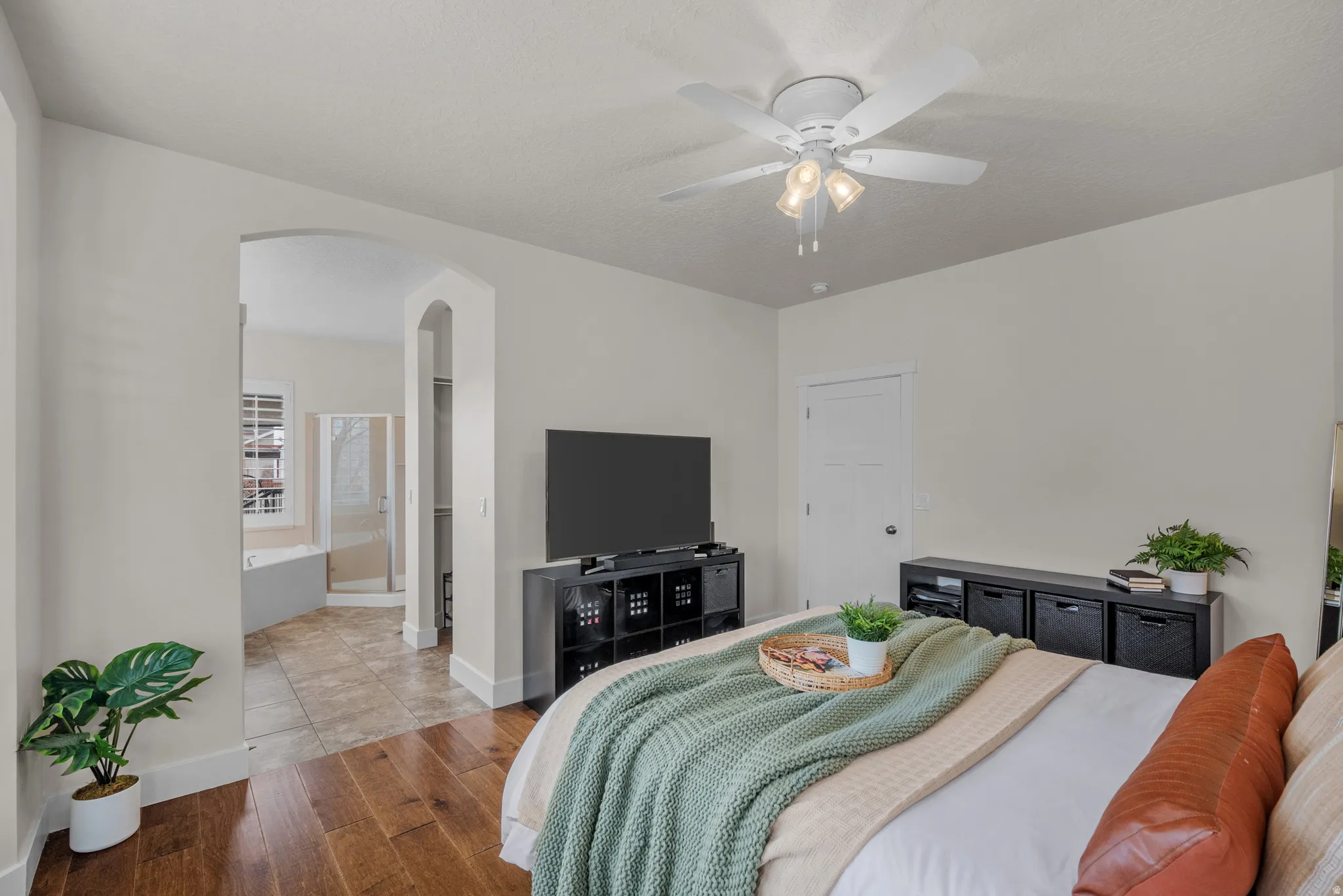 Bedroom with wood finished floors, arched walkways, ceiling fan, and ensuite bath