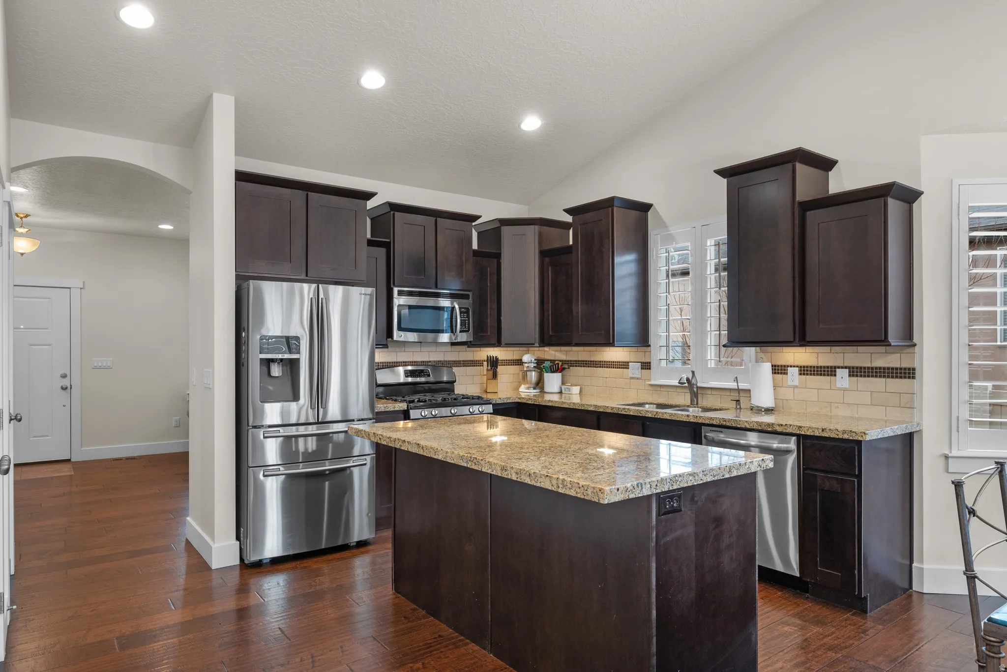 Kitchen with dark wood finish cabinetry, stainless steel appliances, arched walkways, dark wood-type flooring, and lofted ceiling