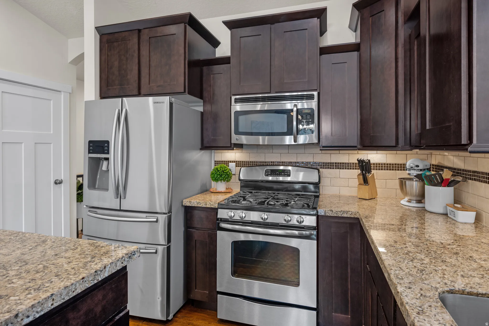 Kitchen featuring stainless steel appliances, dark wood finish cabinets, light stone countertops, and dark wood-type flooring