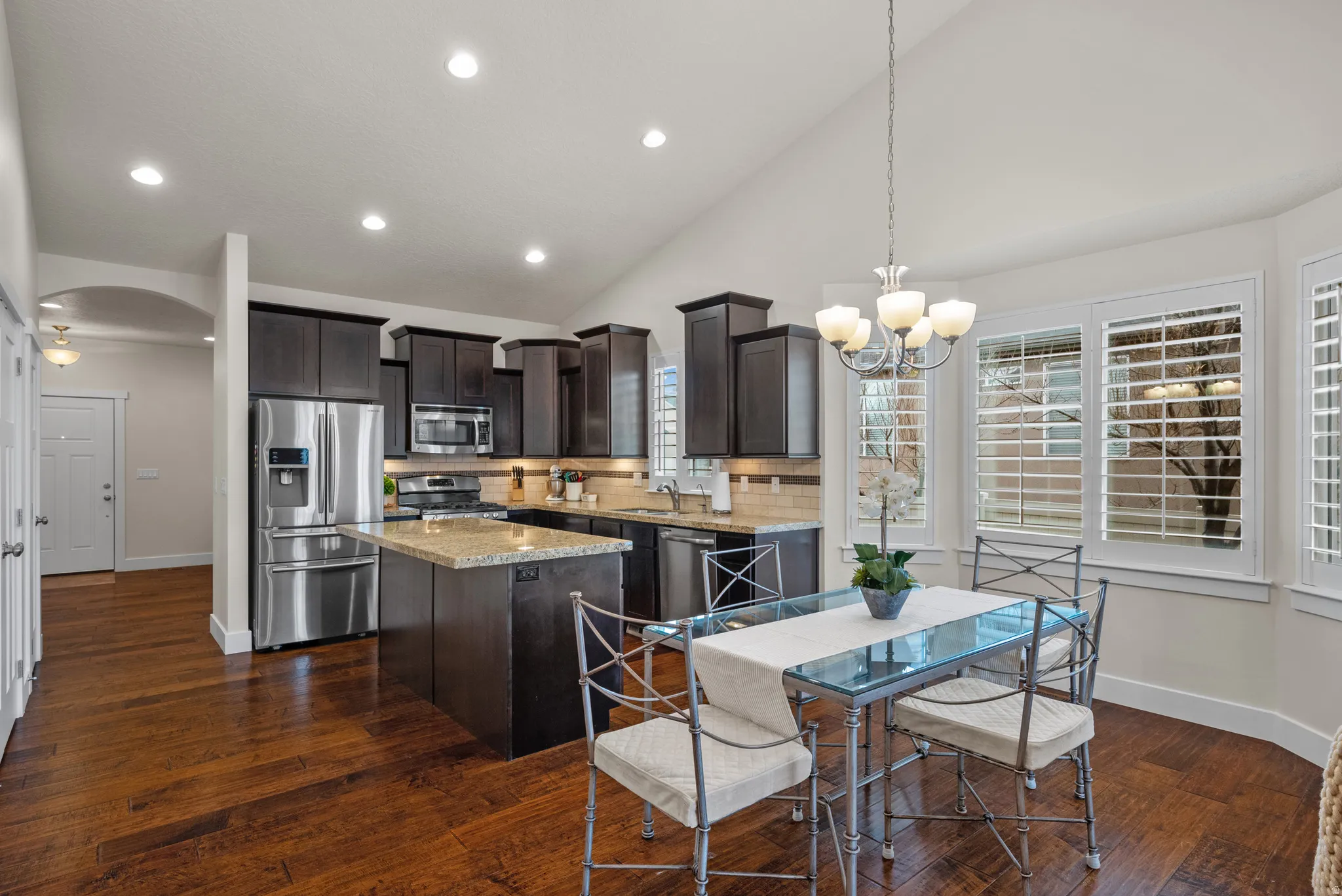 Kitchen featuring dark wood finish cabinets, a center island, stainless steel appliances, lofted ceiling, and light stone counters