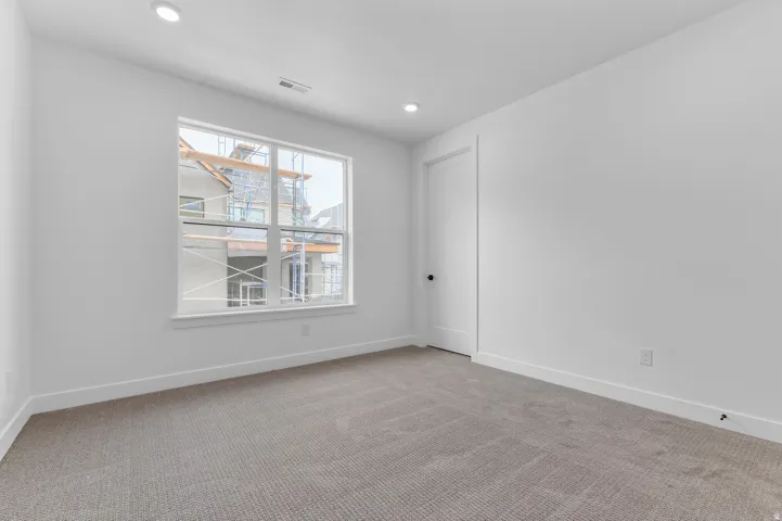 Carpeted room with a large window, recessed lighting, and a white paneled door with a black knob