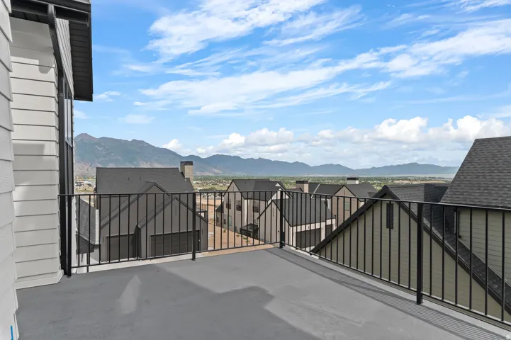 Spacious outdoor balcony with a black metal railing and a grey surface, offering expansive mountain and distant water scenery