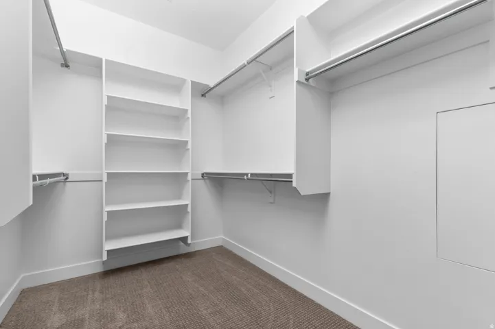 Walk-in closet featuring built-in shelving, multiple hanging rods, white walls, white baseboards, and carpeted flooring