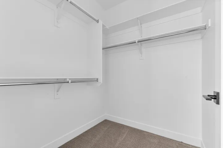 Walk-in closet featuring white walls, white shelving, and hanging rods