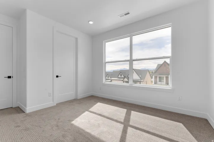 Bright interior space featuring a large window with white framing, white walls, and neutral-toned carpeting
