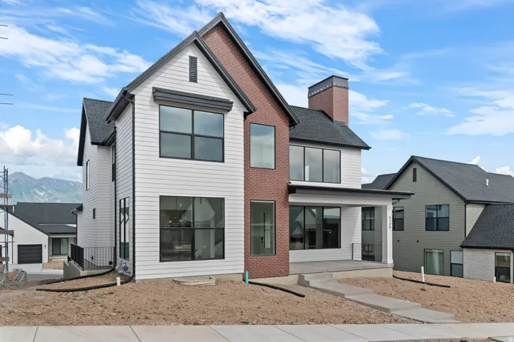 Contemporary exterior featuring white horizontal siding, red brick accents, black-framed windows, a covered front entry, and a prominent brick chimney