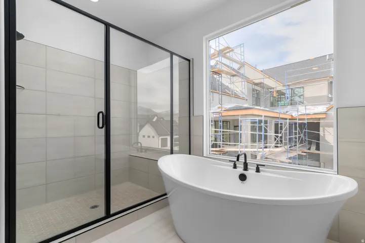 Modern bathroom featuring a freestanding soaking tub with matte black fixtures, a spacious walk-in shower with a glass enclosure and black trim, large format wall tiling, and a large window