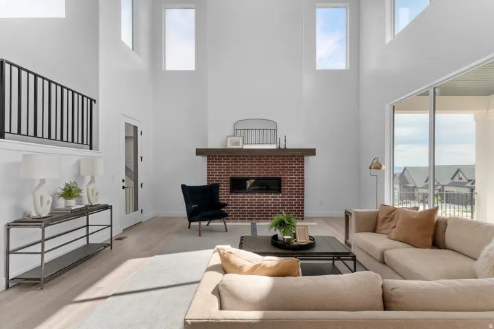 Two-story living area featuring a brick-surround fireplace with a wood mantle, high ceilings, light wood-finish flooring, a full-light glass door, and large-format sliding glass doors