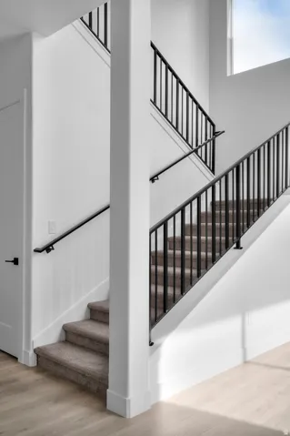 Multilevel staircase featuring wrought iron railings, carpeted treads, and a light wood-finish flooring
