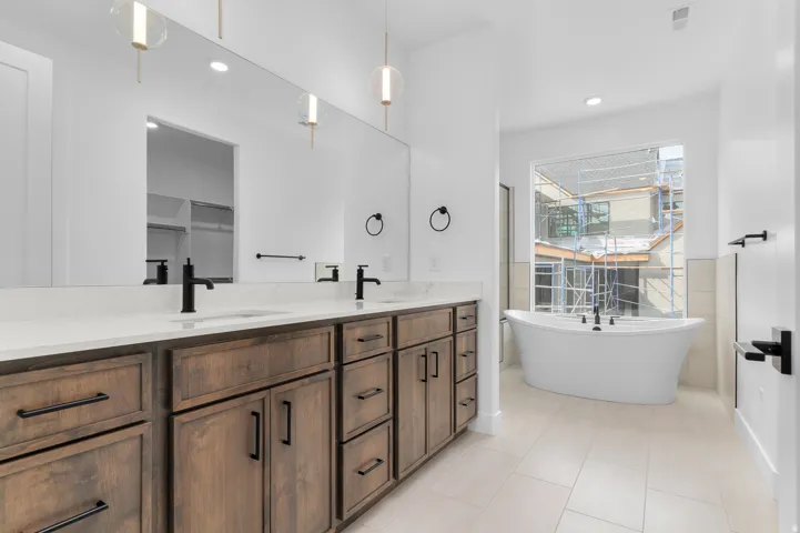 Spacious bathroom featuring a dual vanity with wood-finish cabinetry, white countertops, and matte black fixtures
