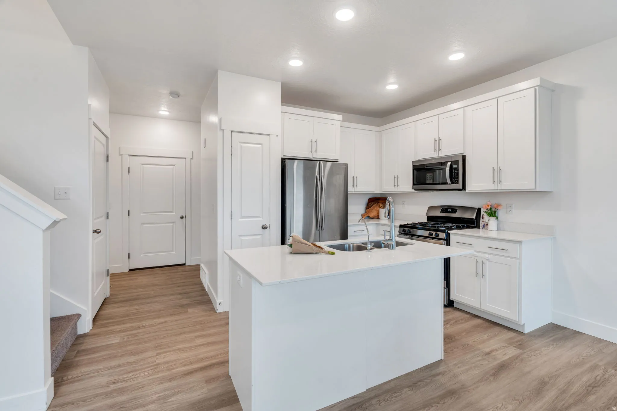 Kitchen featuring stainless steel appliances, a center island with sink, white cabinetry, light wood-style flooring, and recessed lighting