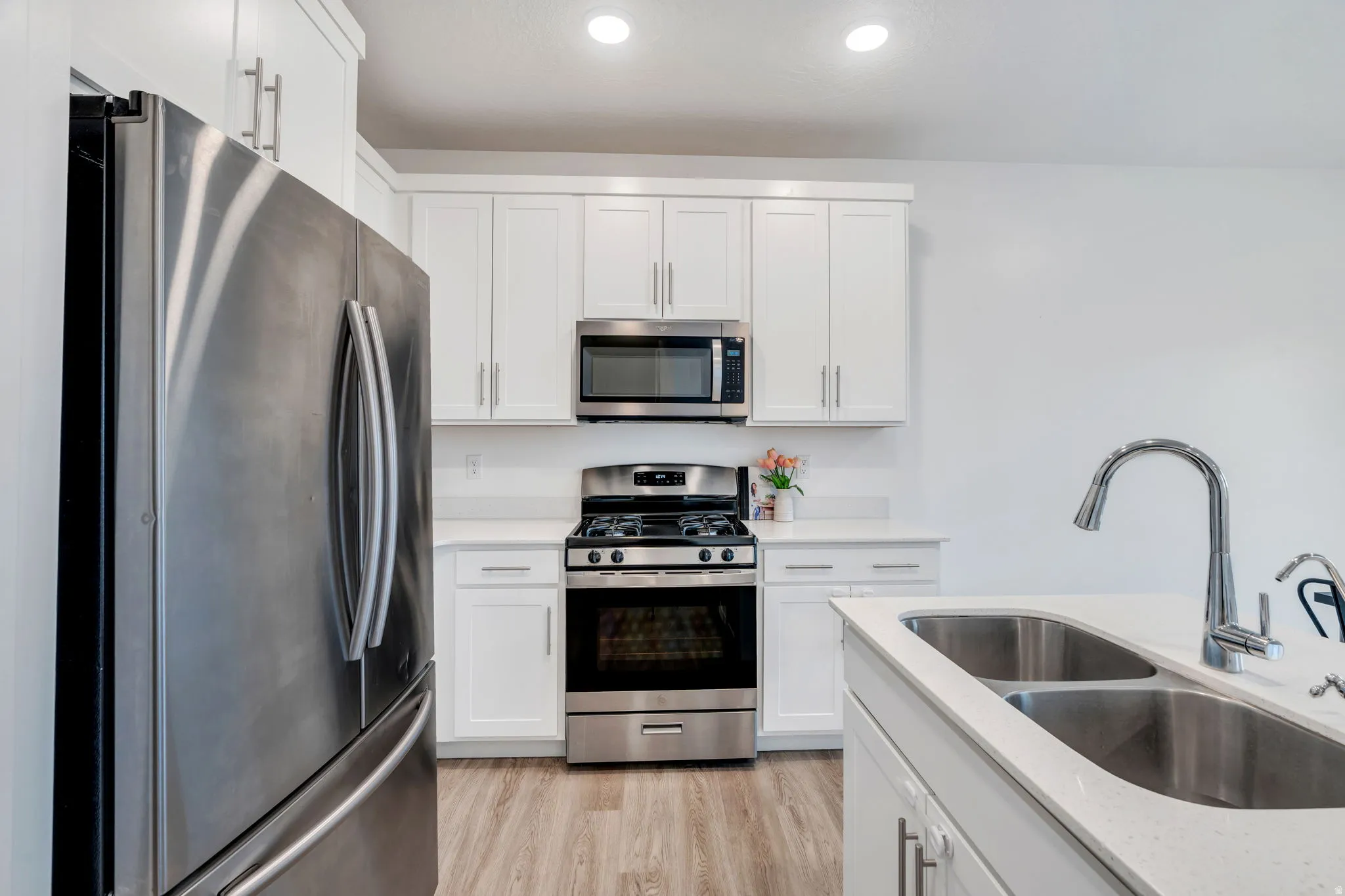 Kitchen with stainless steel appliances, white cabinets, light wood-style flooring, light stone counters, and recessed lighting
