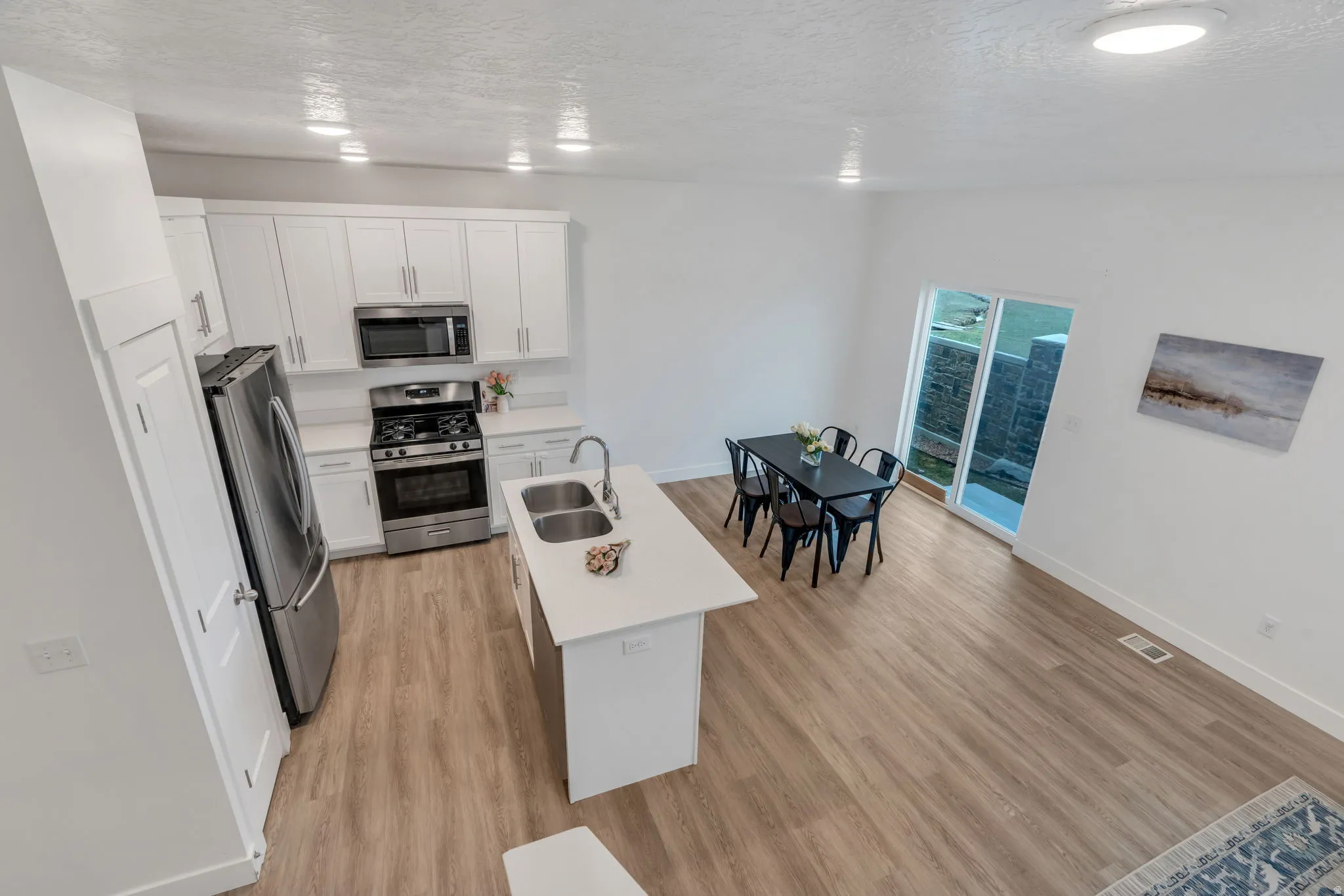 Kitchen featuring stainless steel appliances, a center island with sink, a textured ceiling, light wood-style flooring, and white cabinetry