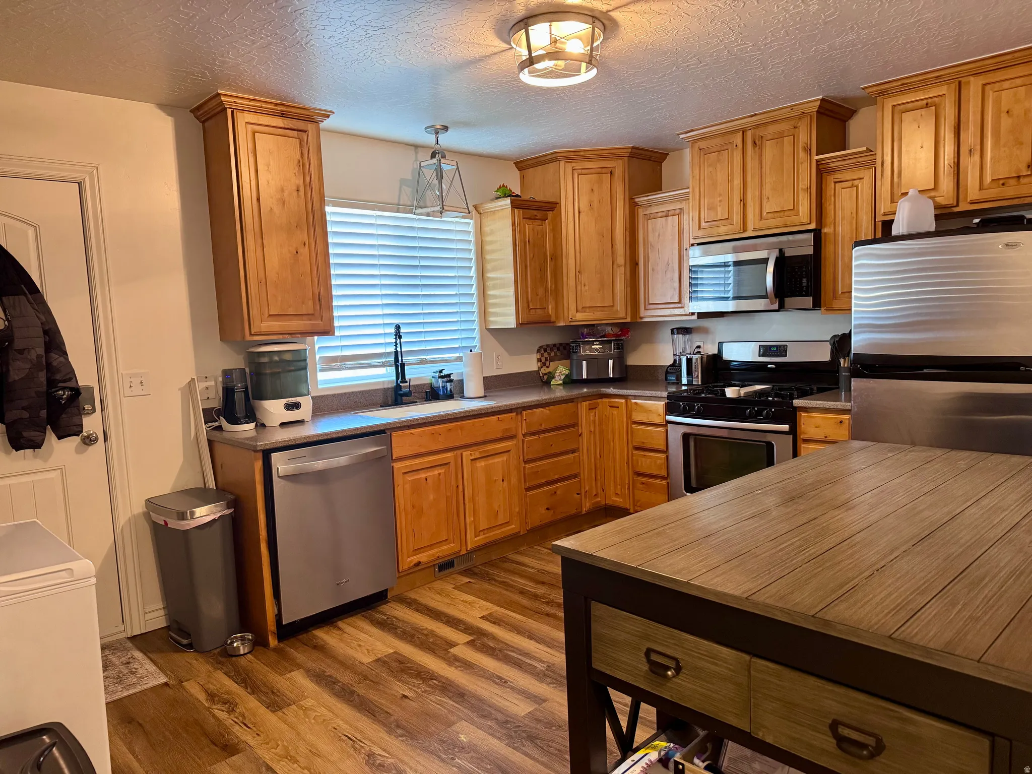 Kitchen with stainless steel appliances, dark countertops, a textured ceiling, dark wood finished floors, and wood finish cabinets