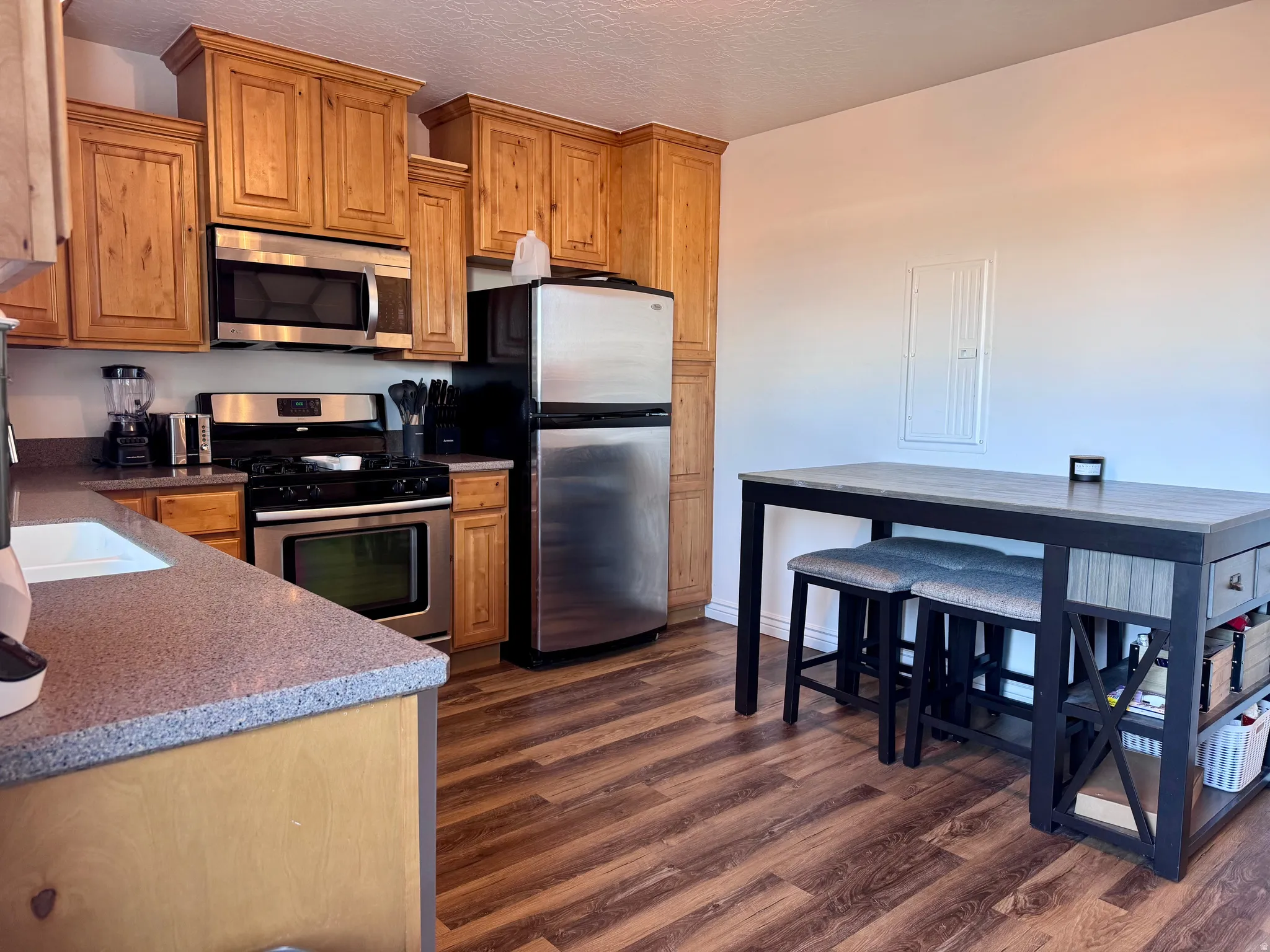 Kitchen with stainless steel appliances, dark wood-type flooring, a textured ceiling, and dark stone countertops