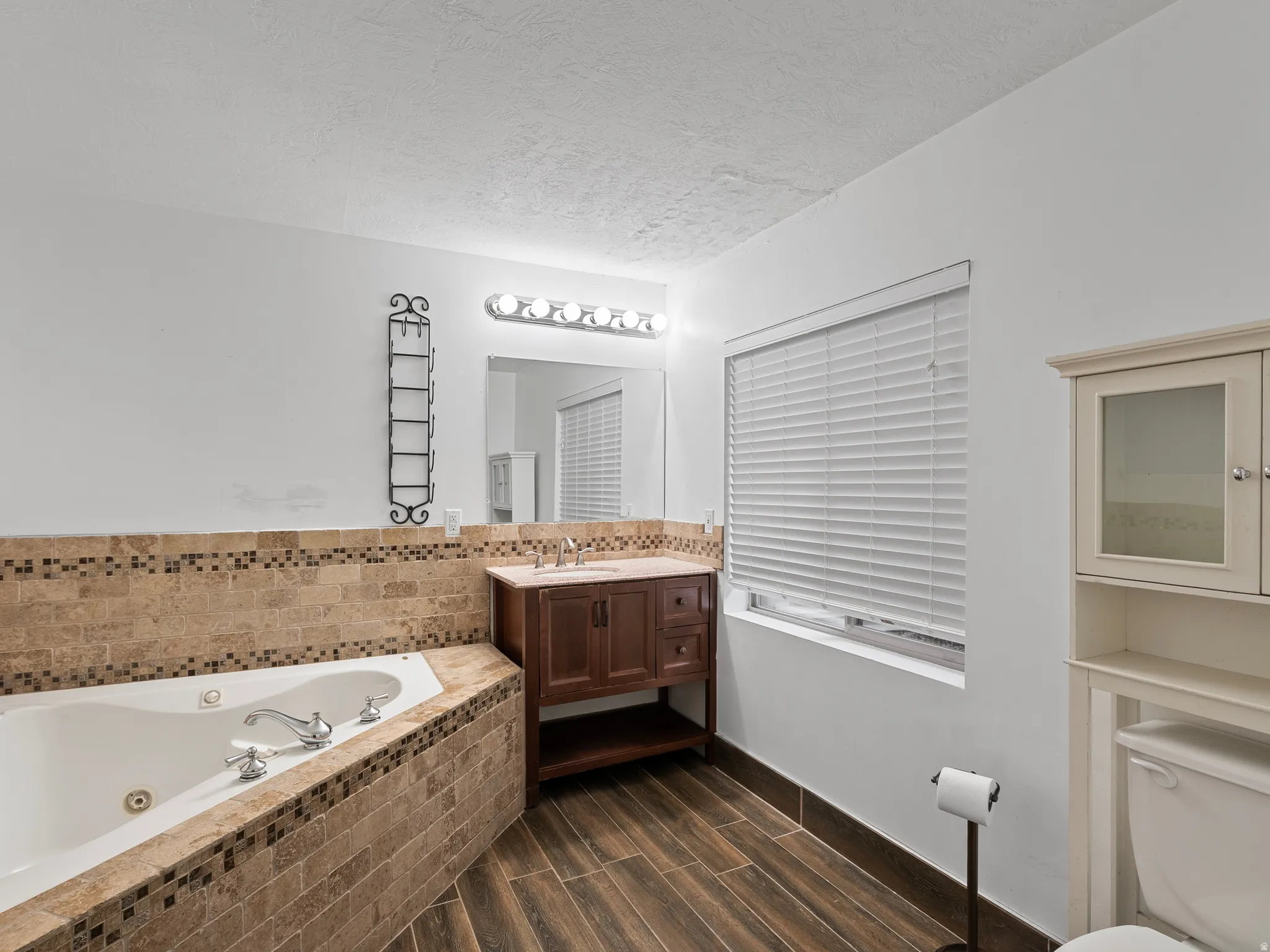 Bathroom with vanity, a tub with jets, wood finish floors, and a textured ceiling