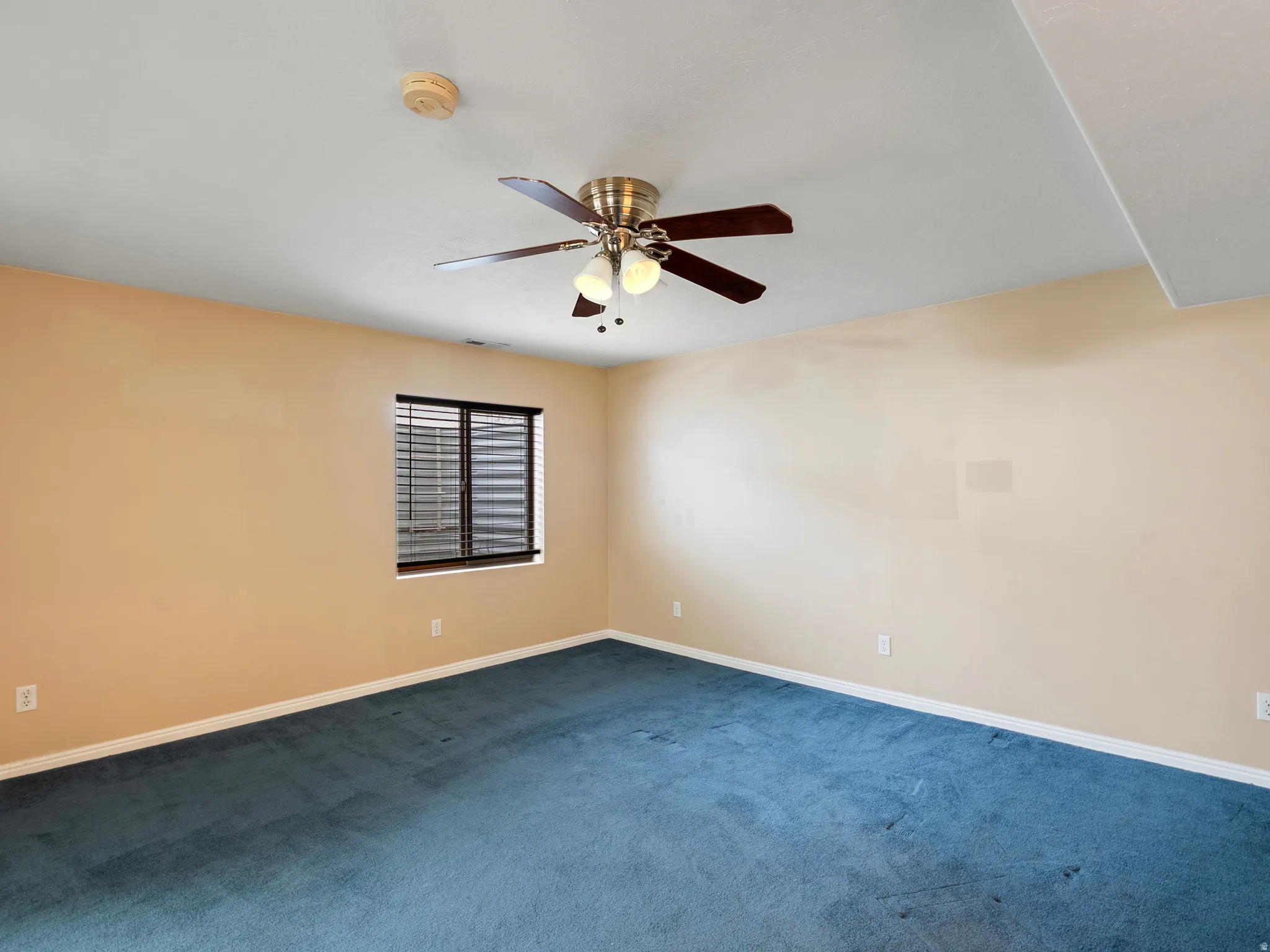 Empty room with a ceiling fan, dark carpet, and a smoke detector