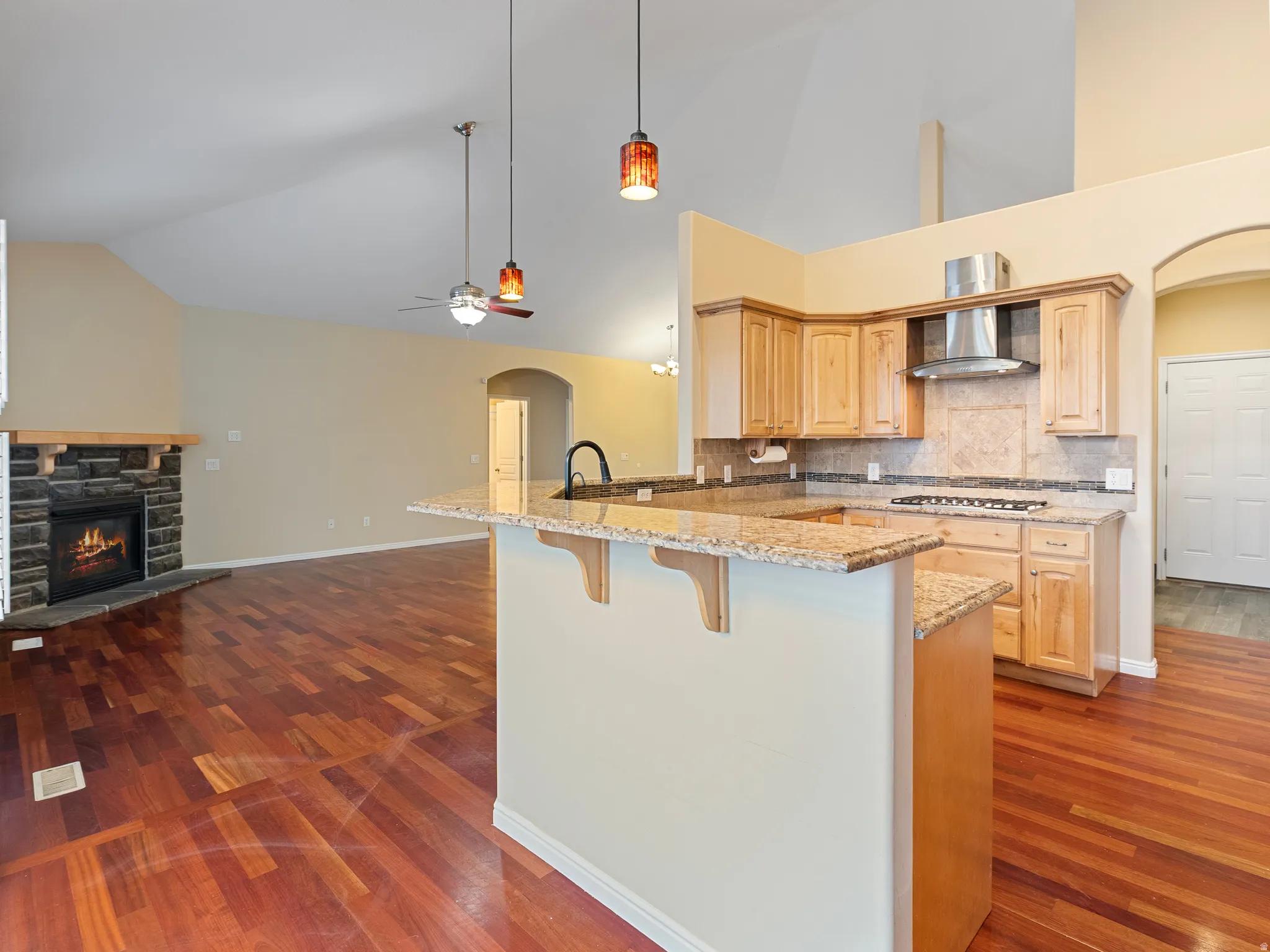 Kitchen featuring arched walkways, a peninsula, light wood finish cabinets, a breakfast bar area, and light stone countertops