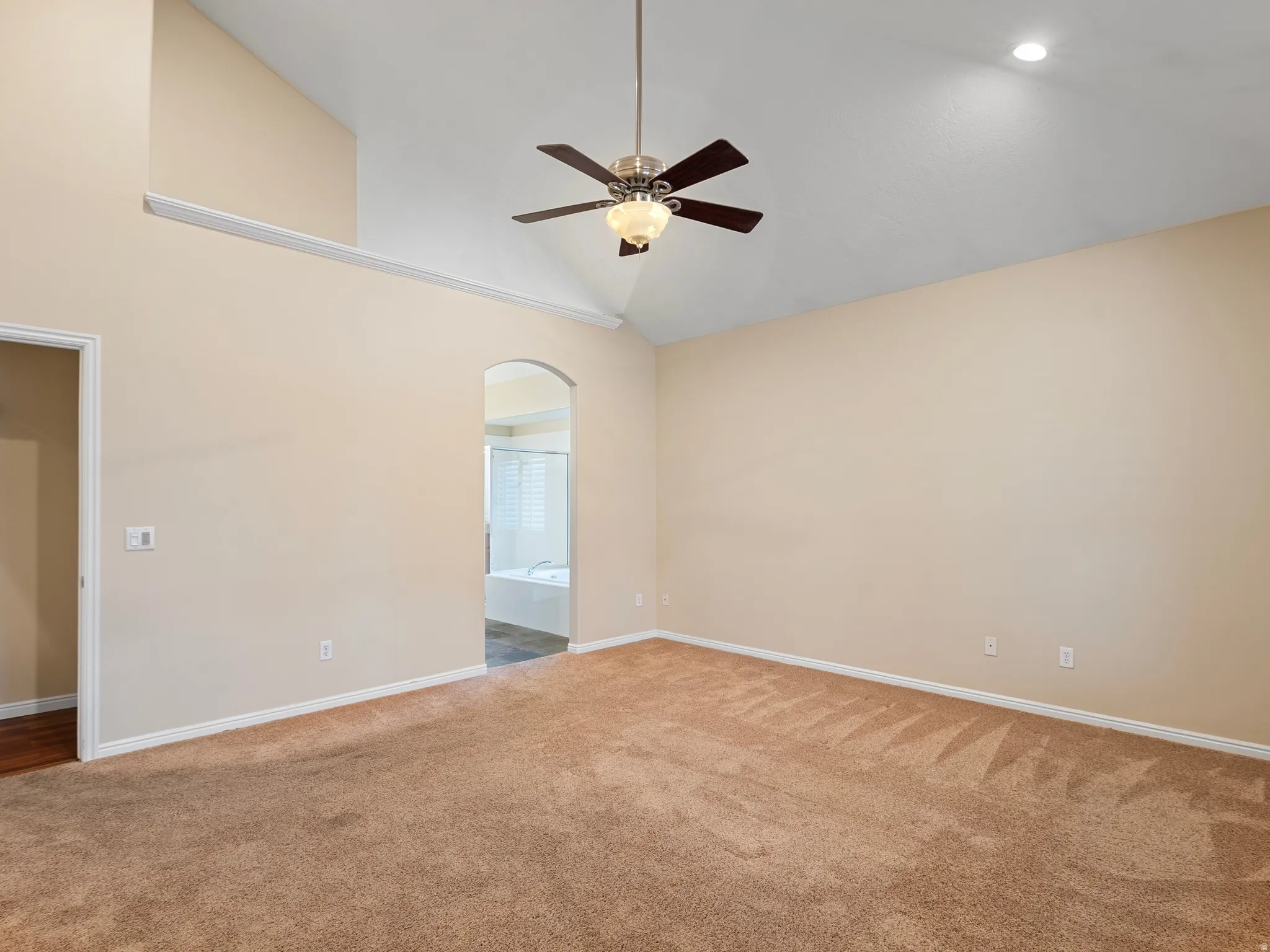 Carpeted spare room with ceiling fan, vaulted ceiling, and arched walkways