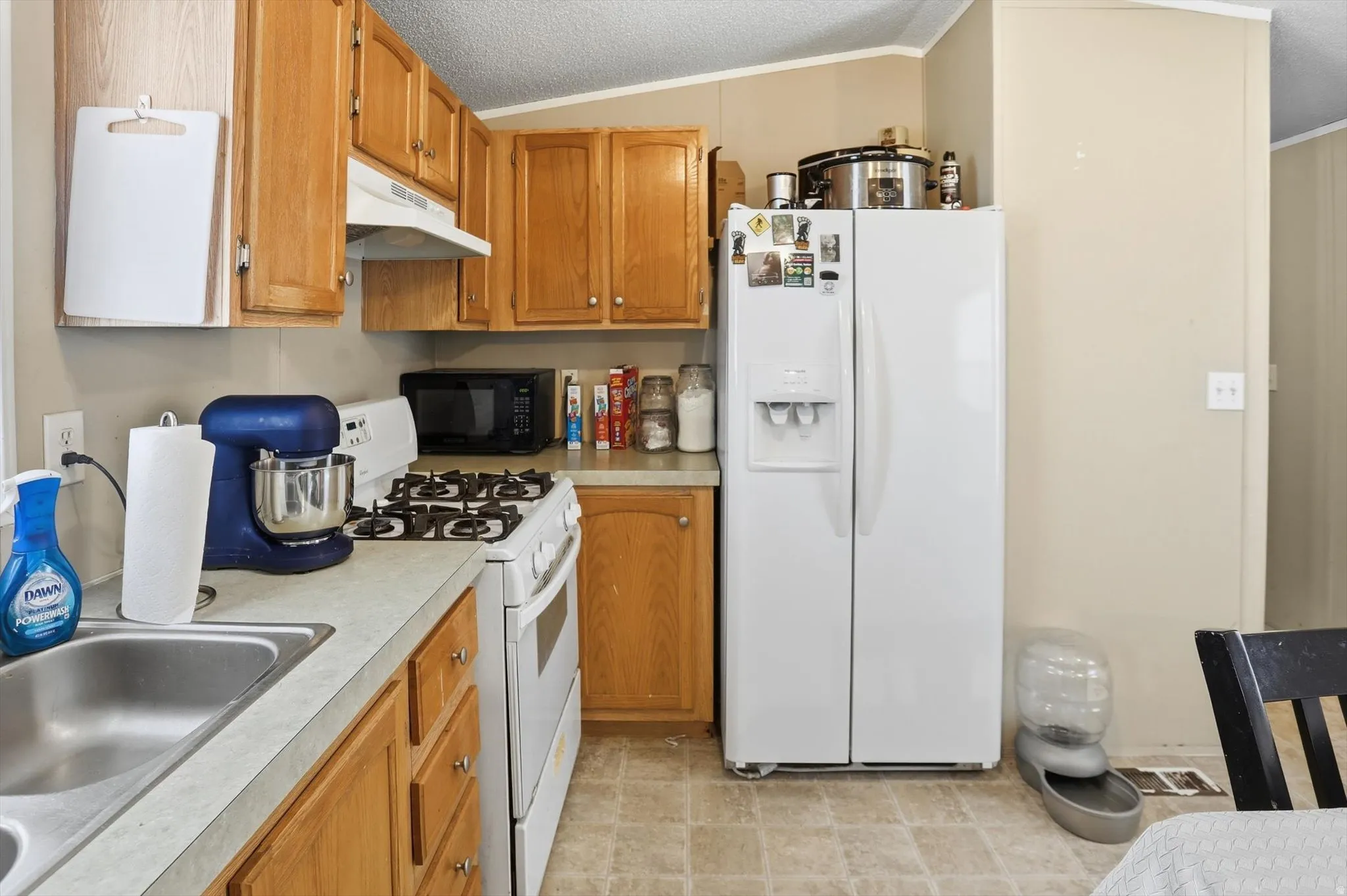 Kitchen featuring white appliances, wood finish cabinetry, light countertops, and crown molding