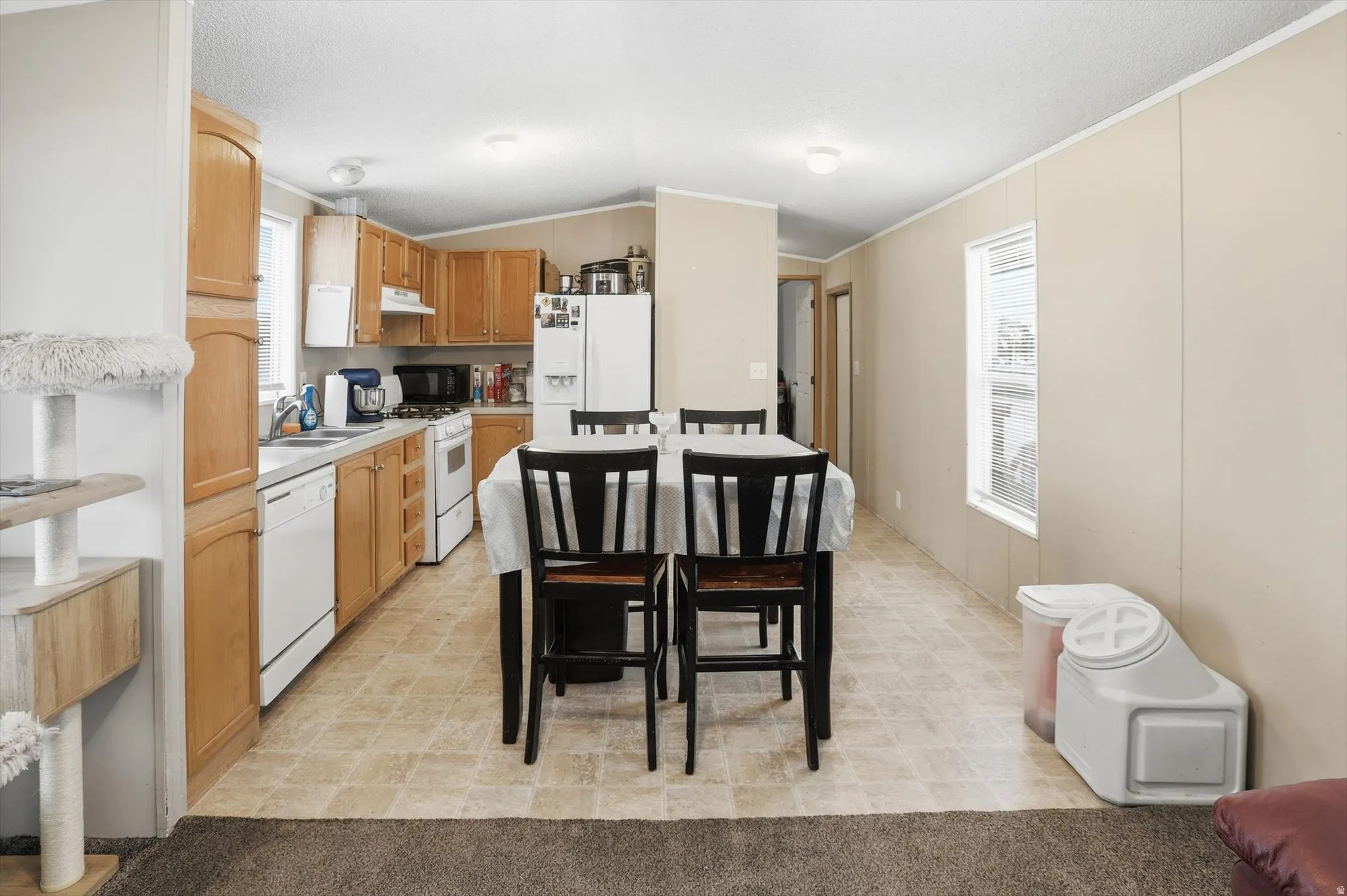 Kitchen with light countertops, white appliances, plenty of natural light, light wood finish cabinets, and vaulted ceiling