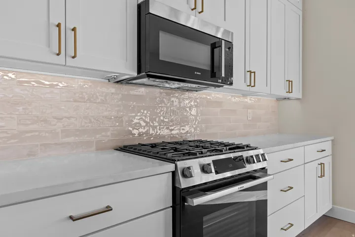 Kitchen featuring stainless steel appliances, white cabinets, light stone countertops, and backsplash