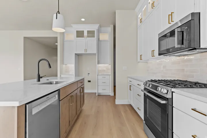 Kitchen with two tone cabinetry, stainless steel appliances, glass insert cabinets, light stone counters, and light wood finished floors