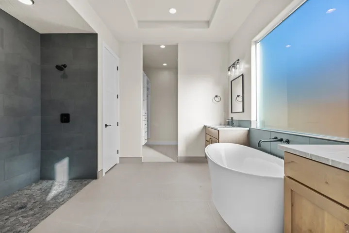Bathroom featuring vanity, a soaking tub, a walk in shower, recessed lighting, and a tray ceiling