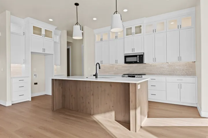 Two tone kitchen featuring glass insert cabinets, a kitchen island with sink, decorative backsplash, dual tone cabinets, and pendant lighting