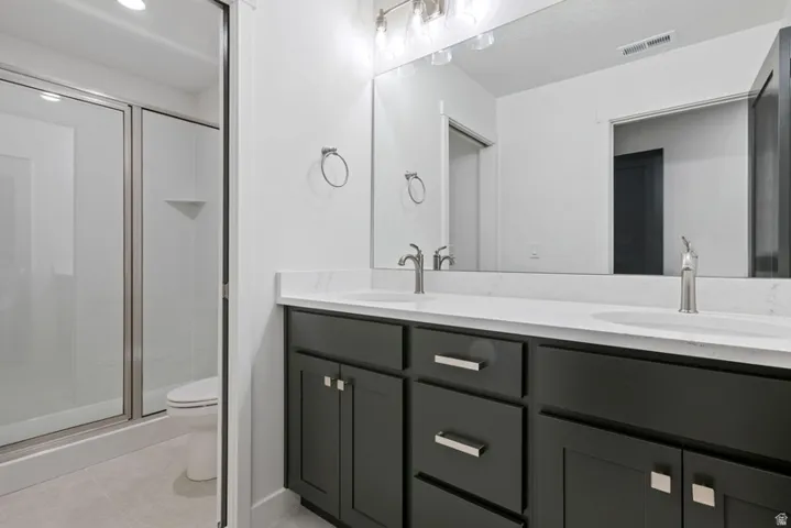 Full bath with double vanity, a stall shower, and light tile patterned flooring