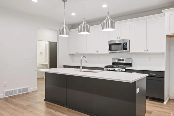 Kitchen featuring two tone color scheme, stainless steel appliances, a center island with sink, light wood-style flooring, and light stone counters