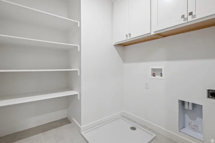 Laundry area with hookup for a washing machine, light tile patterned flooring, hookup for an electric dryer, and cabinet space