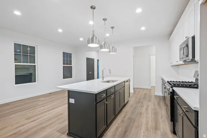 Two tone kitchen featuring stainless steel appliances, a center island with sink, pendant lighting, two tone cabinets, and light stone countertops