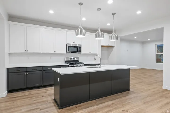 Dual tone kitchen featuring dual tone cabinetry, stainless steel appliances, hanging light fixtures, decorative backsplash, and light wood-style flooring