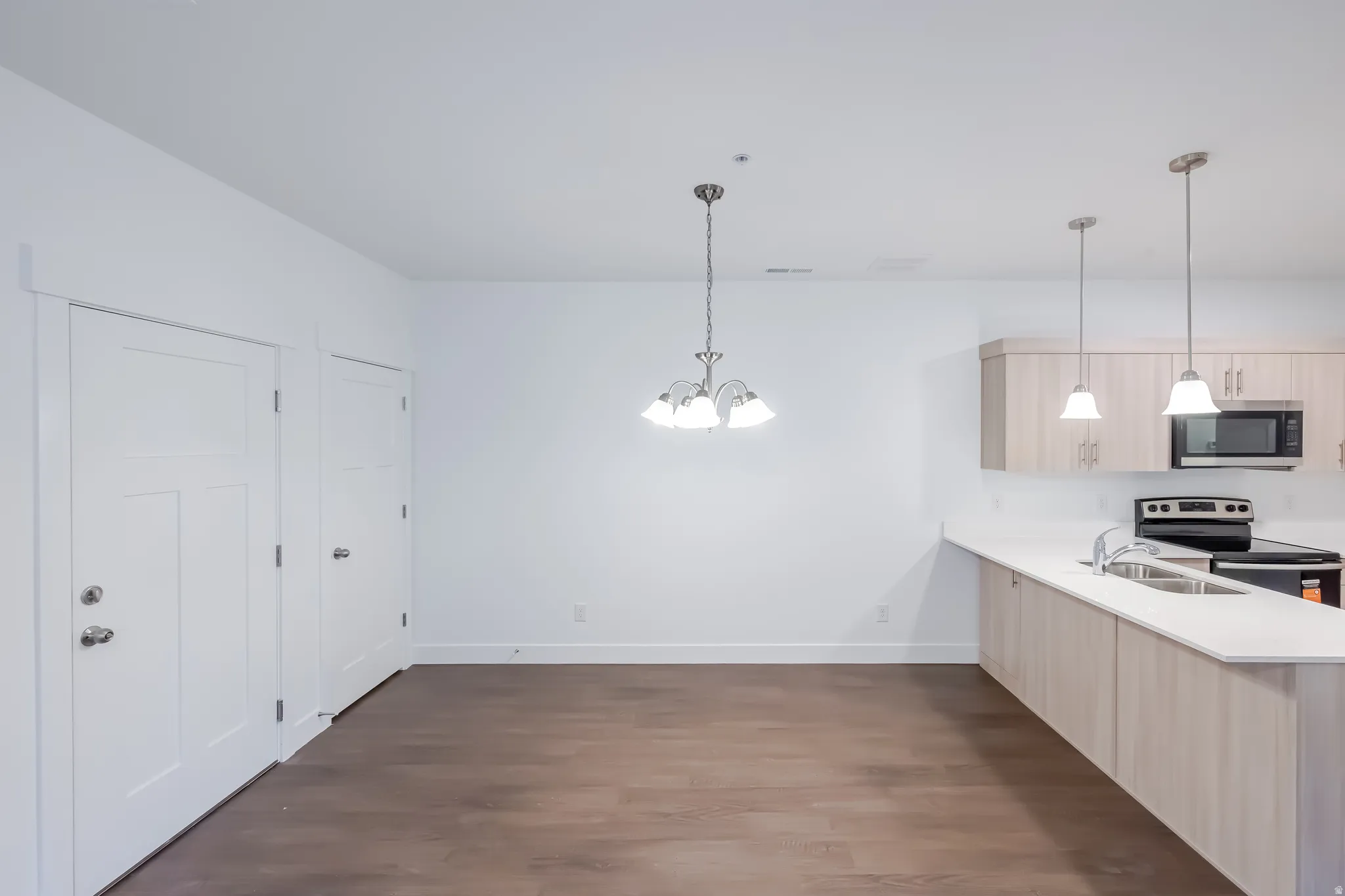 Open-concept layout with wood-finish flooring, white walls, and a contemporary light fixture
