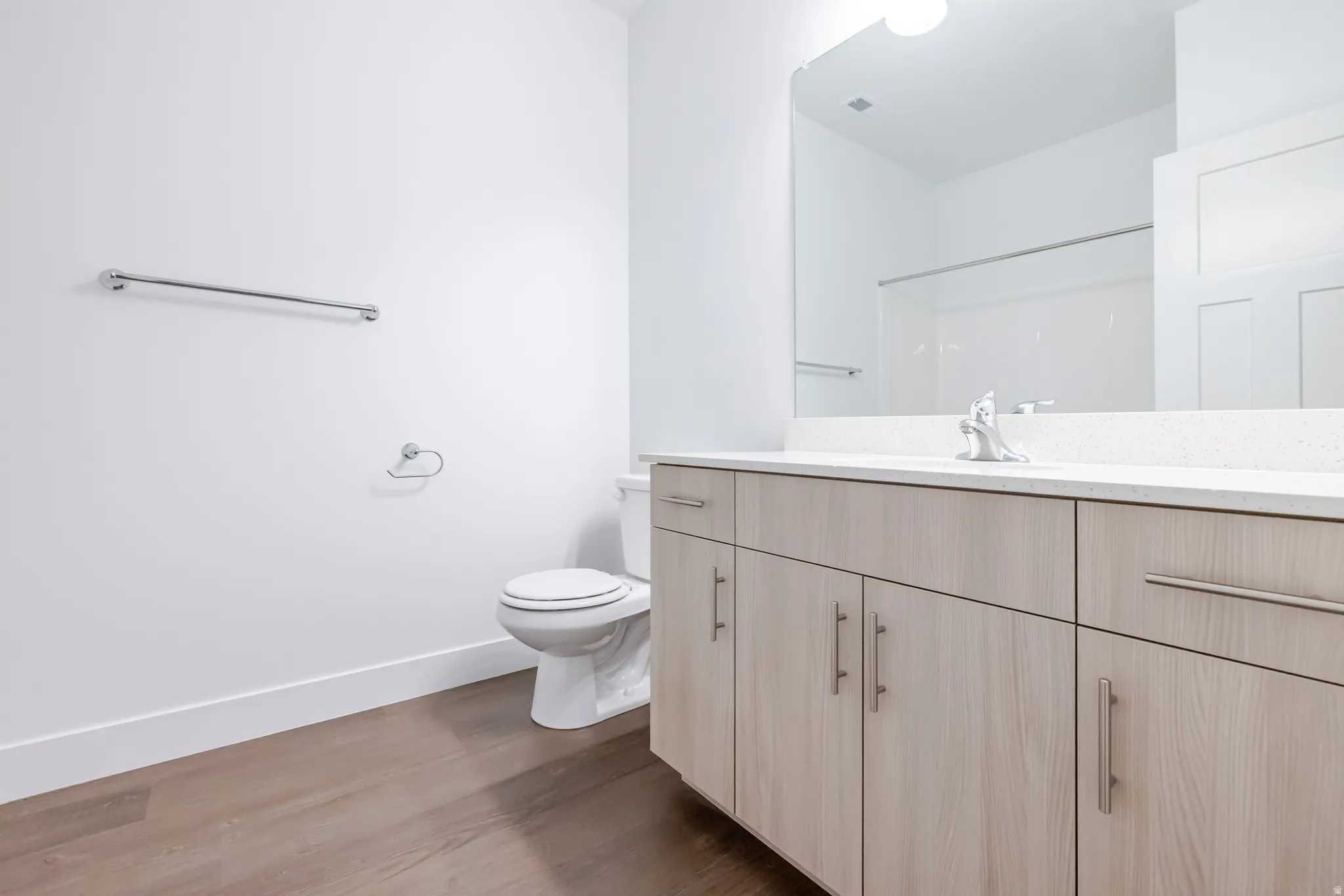 Wood-finish flooring, white walls, and a light wood-finish vanity with chrome hardware