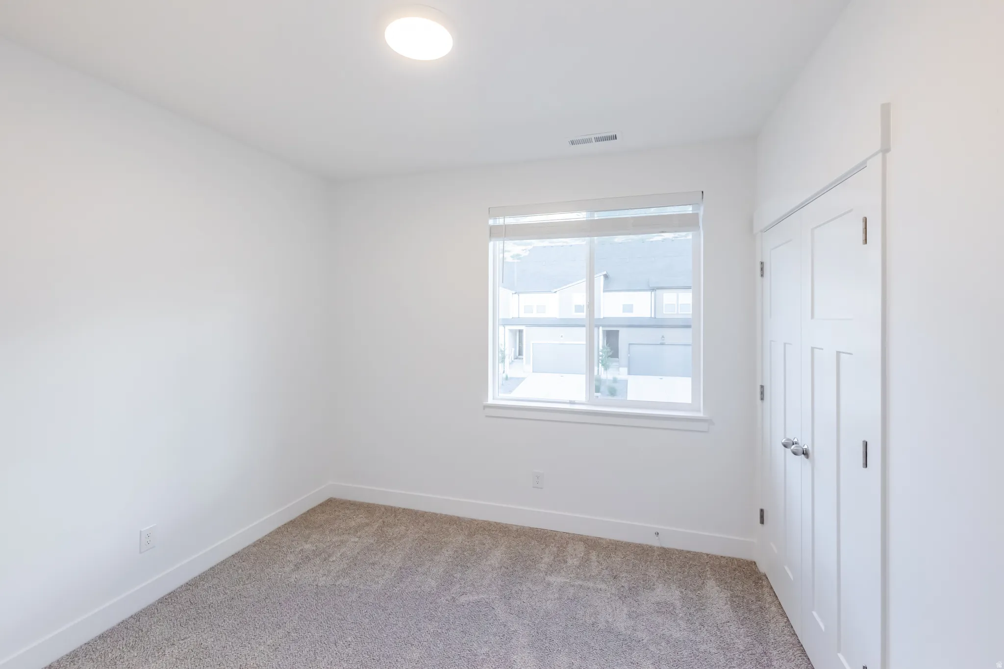 Neutral wall paint, carpet flooring, a single window with blinds, and white paneled doors