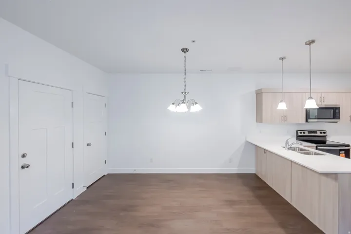 Open-concept layout with wood-finish flooring, white walls, and a contemporary light fixture