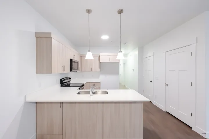 Kitchen featuring wood-finish cabinetry, white countertops, stainless steel appliances, and a double basin sink with a chrome faucet