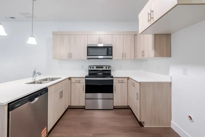 U-shaped kitchen with light wood-finish cabinetry, white countertops, stainless steel appliances, and wood-finish flooring